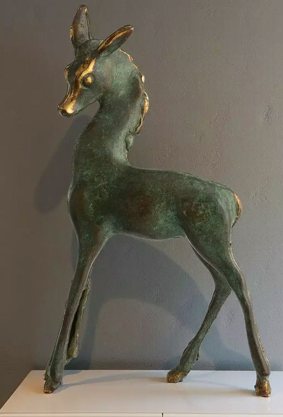 A bronze statue of a deer standing on a white surface against a gray background.